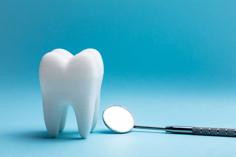 A white tooth next to a dental mirror on a blue background
