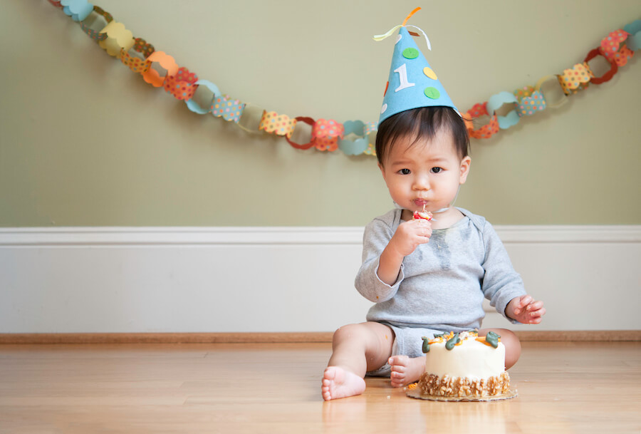 Baby celebrates first birthday with a cake and wears a hat with 1 on it