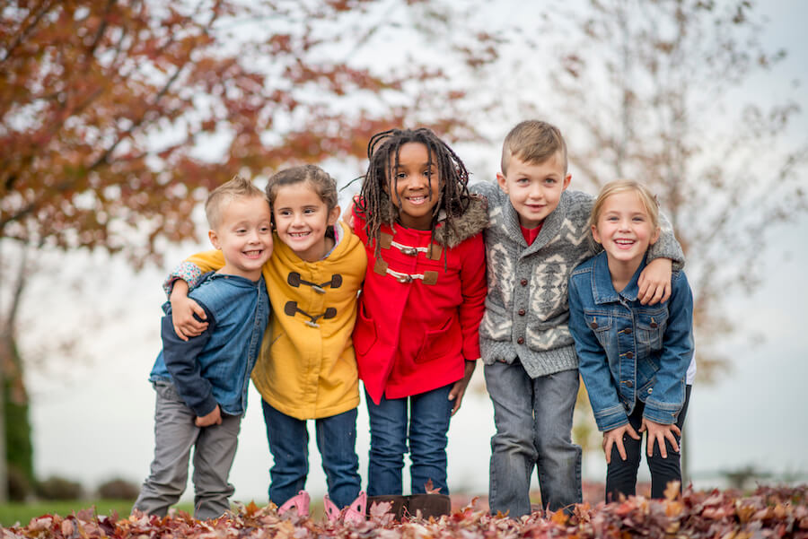 5 children in winter coats smile together with their arms around each other's shoulders