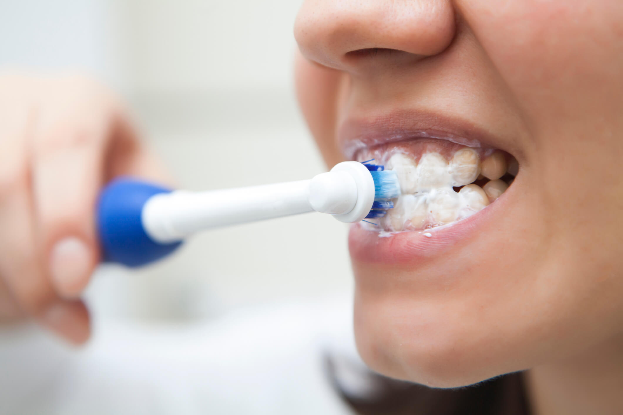 closeup of a woman brushing her teeth with an electric toothbrush