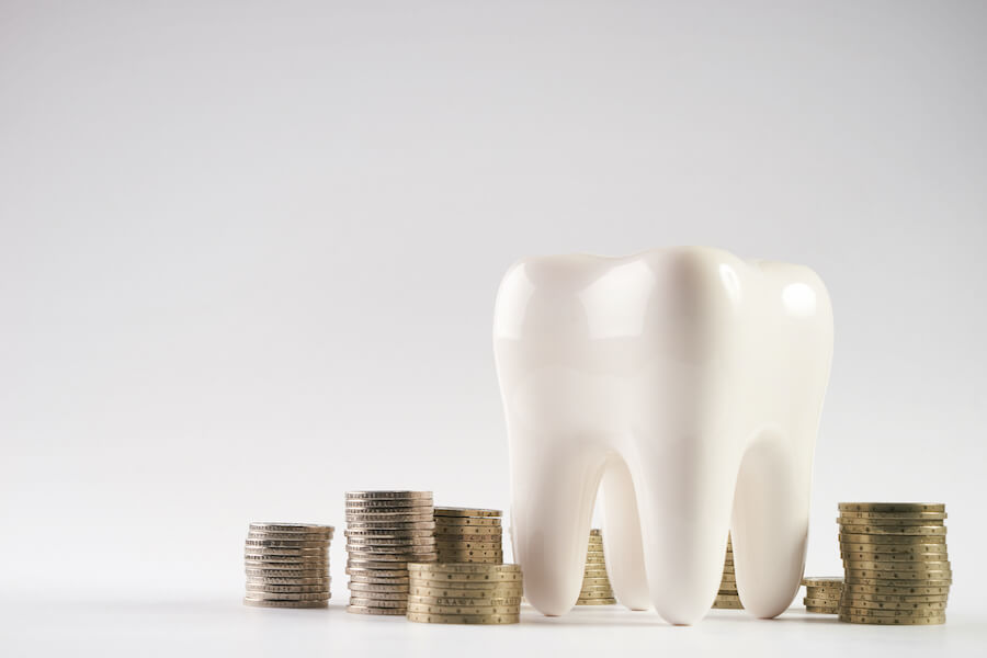 A white tooth next to several piles of coins