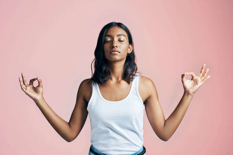 Brown woman relaxes and stands in a zen pose against a pink wall