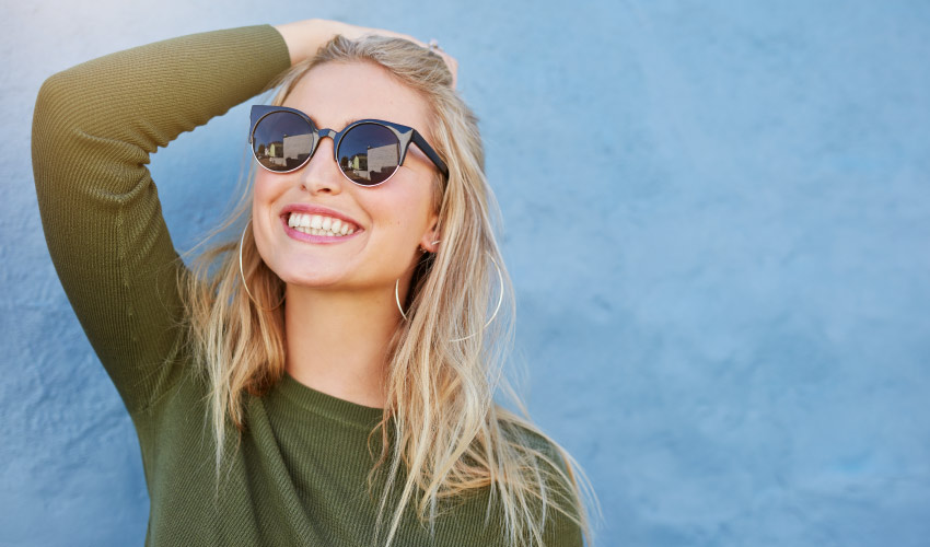 Blonde woman wears a green shirt and sunglasses while outside in the sun