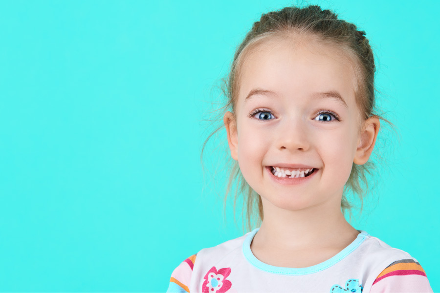 Little girl missing one of her bottom teeth smiles against a bright blue background